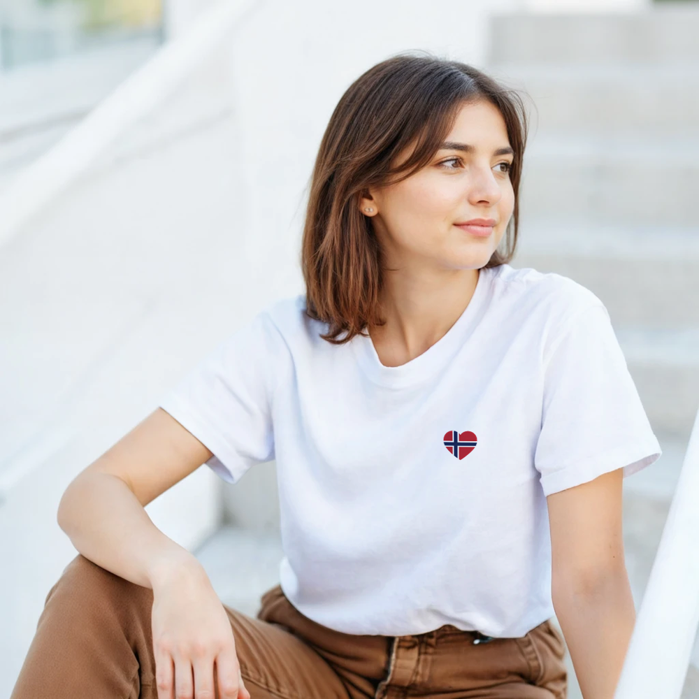 Kvinnelig modell med hvit unisex-t-skjorte fra Gildan 5000, med norsk flagghjerte på venstre bryst.